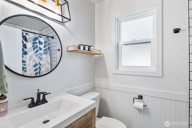 full bathroom with a shower with shower curtain, vanity, toilet, and wainscoting