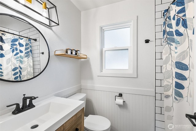 full bath with vanity, a shower with shower curtain, toilet, and a wainscoted wall