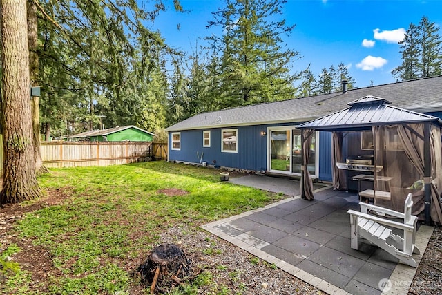 rear view of property featuring fence, roof with shingles, a yard, a gazebo, and a patio area