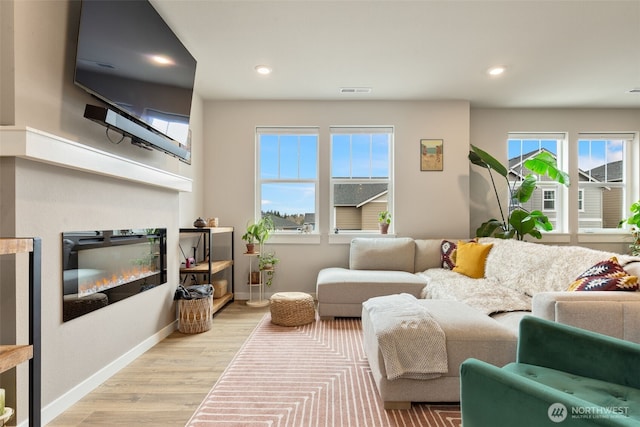 living room featuring light wood finished floors, visible vents, baseboards, recessed lighting, and a glass covered fireplace