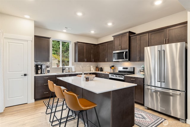 kitchen with light wood-type flooring, a sink, stainless steel appliances, a breakfast bar area, and dark brown cabinets