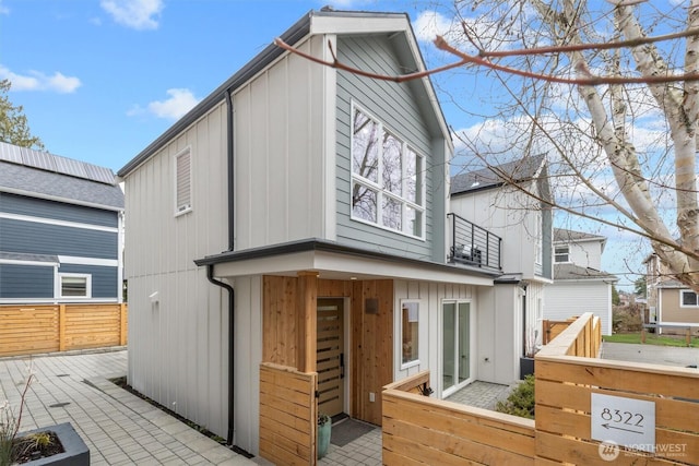 rear view of house featuring a patio, a balcony, fence, and board and batten siding