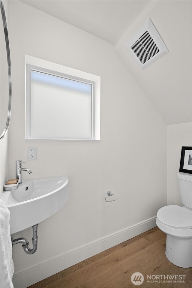 bathroom with wood finished floors, visible vents, baseboards, lofted ceiling, and toilet