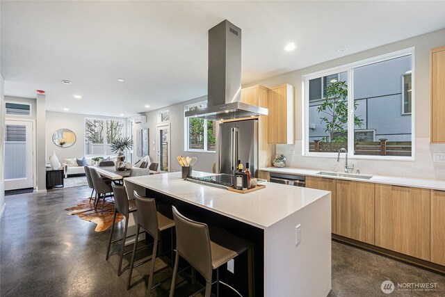 kitchen with island exhaust hood, light brown cabinetry, a sink, appliances with stainless steel finishes, and modern cabinets