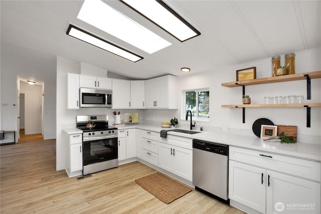 kitchen with a sink, white cabinetry, light wood-style floors, appliances with stainless steel finishes, and lofted ceiling