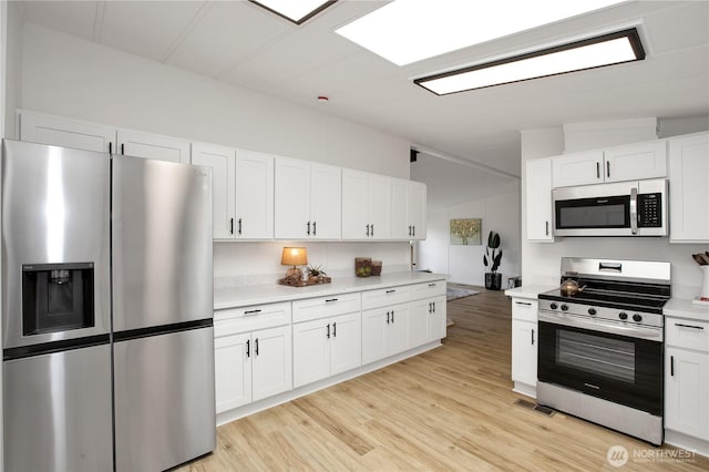 kitchen featuring light wood-style flooring, white cabinetry, appliances with stainless steel finishes, light countertops, and vaulted ceiling