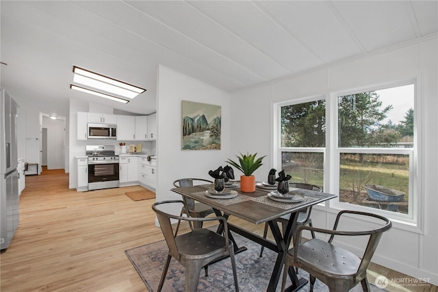 dining area featuring light wood finished floors, baseboards, and vaulted ceiling