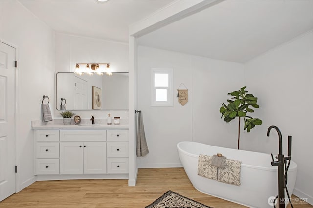 bathroom with wood finished floors, baseboards, a freestanding bath, vanity, and vaulted ceiling