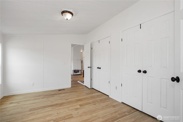 unfurnished bedroom with light wood-type flooring, baseboards, two closets, and visible vents