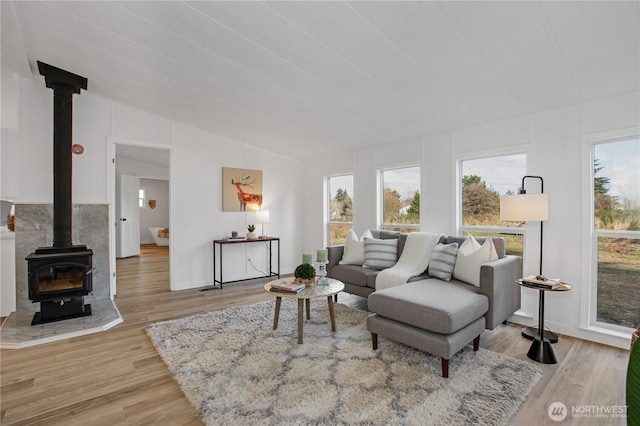 living area with light wood finished floors, a wood stove, and vaulted ceiling