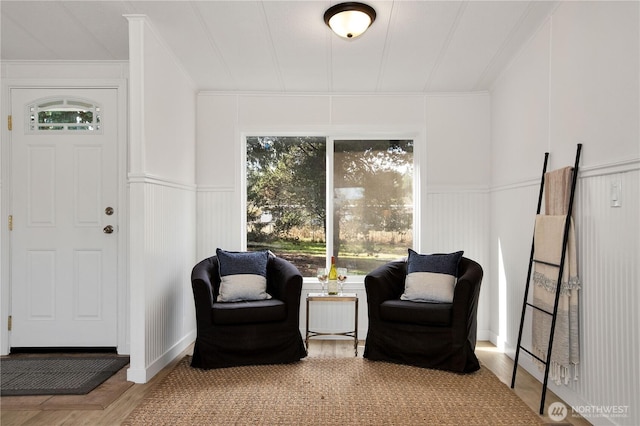 sitting room with a wainscoted wall, wood finished floors, ornamental molding, and a decorative wall