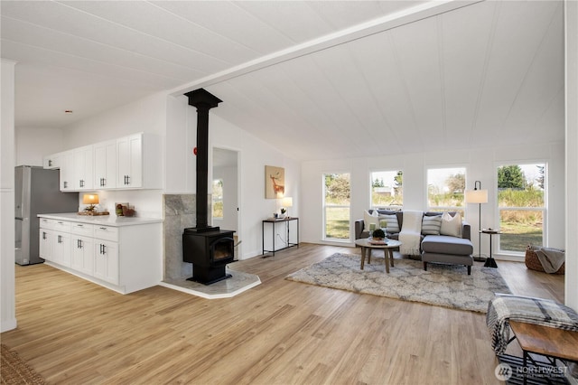 living area featuring lofted ceiling, a wood stove, and light wood-style flooring