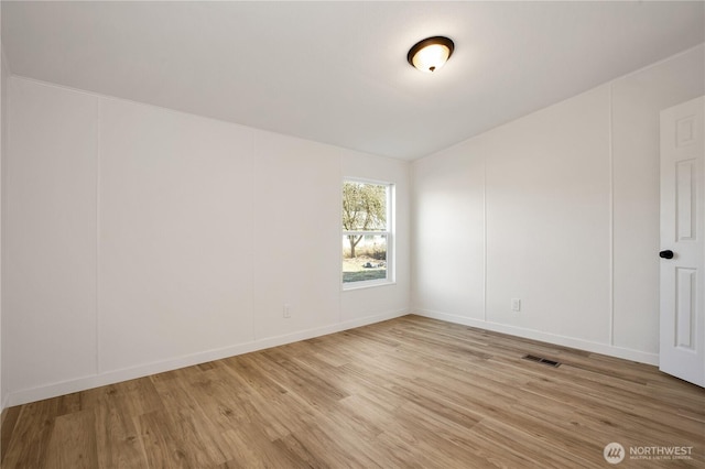 empty room with light wood-type flooring, visible vents, and a decorative wall