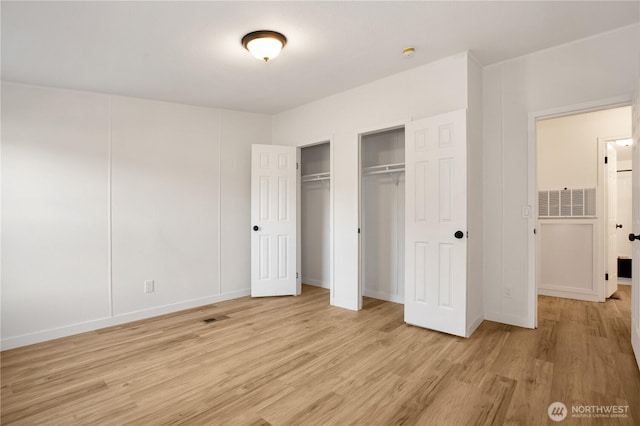 unfurnished bedroom with visible vents, two closets, and light wood finished floors