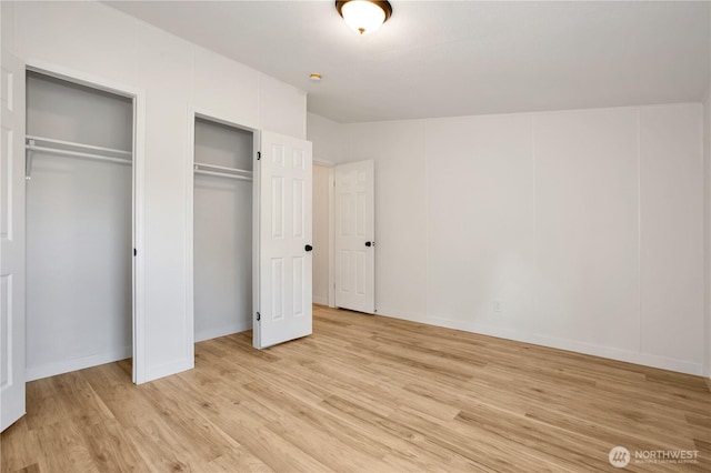 unfurnished bedroom featuring light wood-type flooring and multiple closets