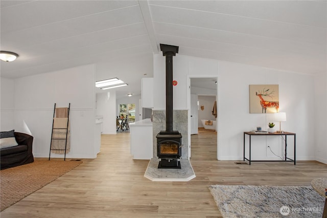 living room featuring baseboards, lofted ceiling, a wood stove, and light wood finished floors