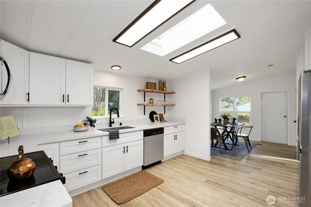 kitchen with vaulted ceiling with skylight, appliances with stainless steel finishes, white cabinets, and a sink