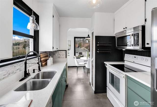 kitchen with white electric stove, arched walkways, a sink, stainless steel microwave, and backsplash