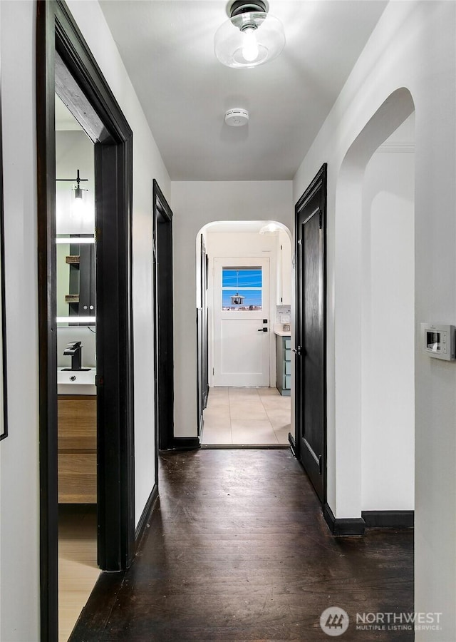 hallway featuring a sink, light wood-type flooring, arched walkways, and baseboards