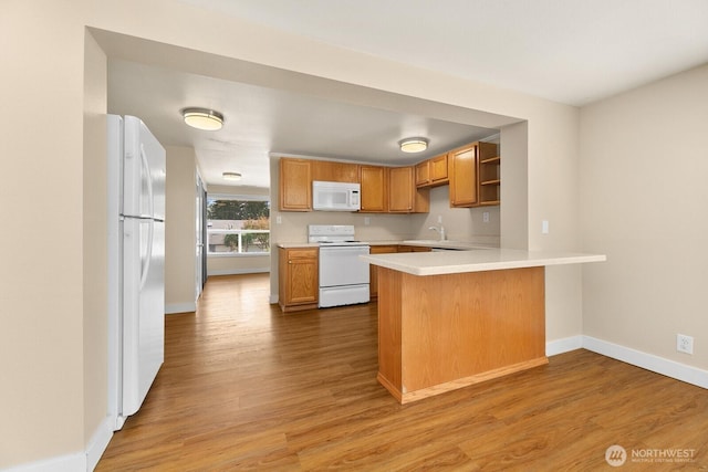 kitchen featuring white appliances, wood finished floors, baseboards, a peninsula, and light countertops