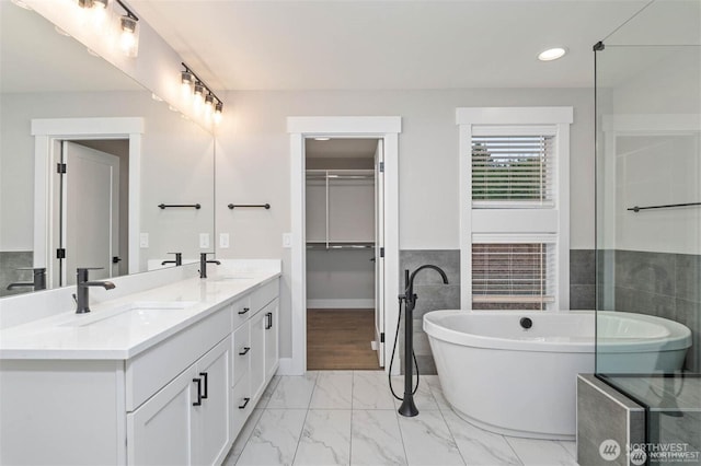 bathroom featuring a sink, a freestanding bath, marble finish floor, and double vanity