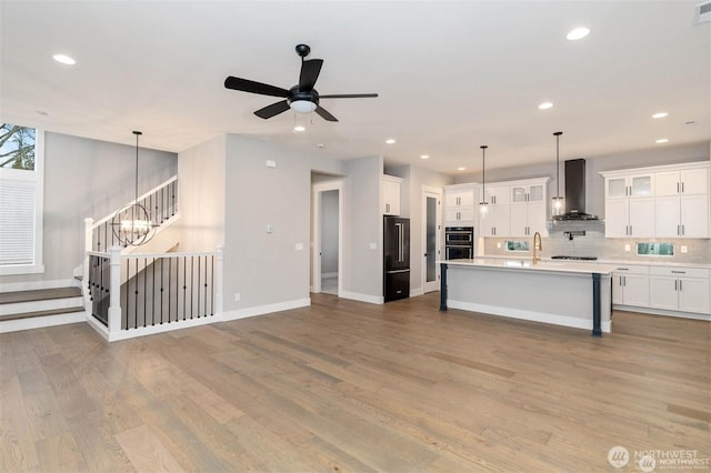 kitchen with backsplash, double oven, light countertops, high end black refrigerator, and wall chimney exhaust hood