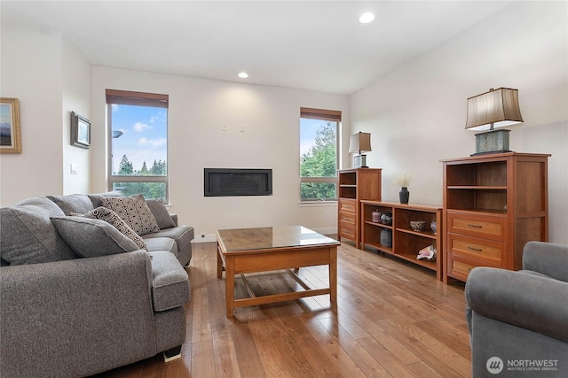 living area with a glass covered fireplace, recessed lighting, and light wood-type flooring