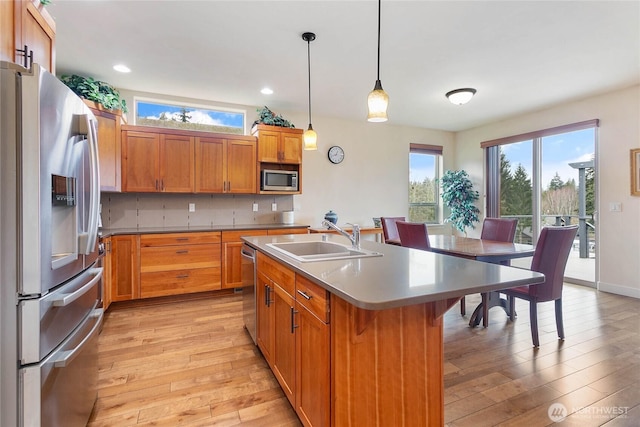 kitchen with a sink, stainless steel appliances, light wood-type flooring, and a kitchen island with sink