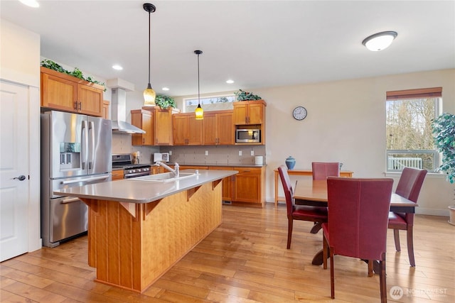 kitchen with wall chimney range hood, light wood-style flooring, appliances with stainless steel finishes, and a sink