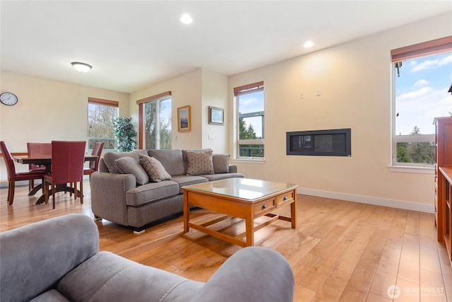 living room featuring recessed lighting, light wood-type flooring, baseboards, and a glass covered fireplace