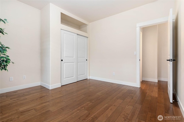 unfurnished bedroom with dark wood finished floors, baseboards, and a closet