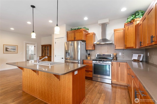 kitchen with light wood-type flooring, a sink, backsplash, appliances with stainless steel finishes, and wall chimney exhaust hood