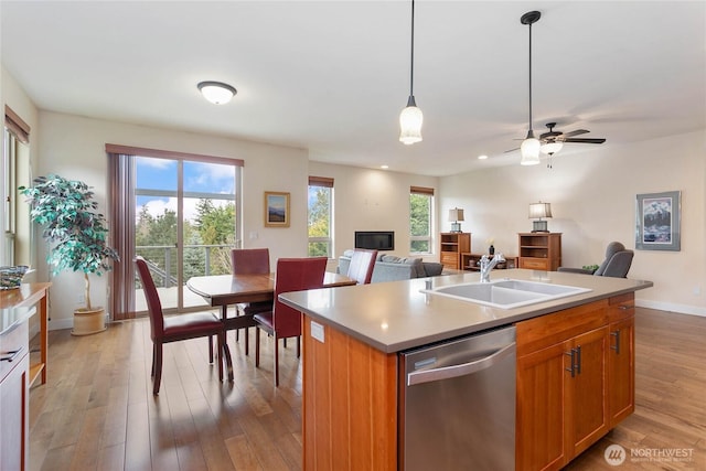 kitchen with a healthy amount of sunlight, open floor plan, light wood-type flooring, stainless steel dishwasher, and a sink