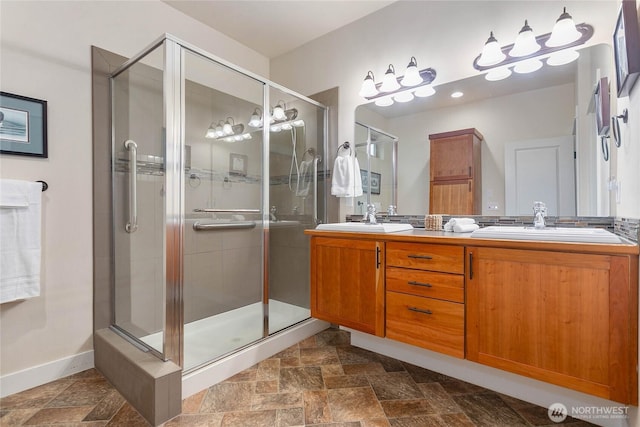 full bathroom featuring a shower stall, stone finish flooring, double vanity, and a sink