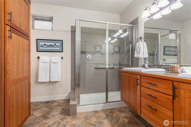 full bath featuring vanity, a shower stall, baseboards, and stone tile flooring