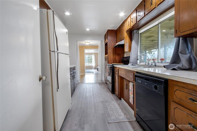 kitchen featuring light countertops, a sink, under cabinet range hood, black appliances, and light wood-style floors