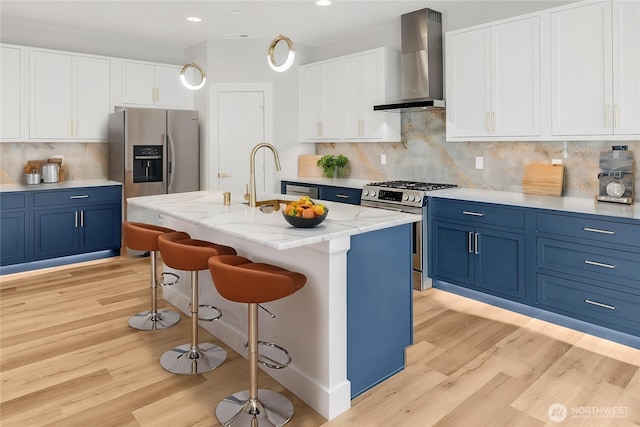 kitchen with wall chimney exhaust hood, stainless steel appliances, blue cabinets, light wood-style floors, and recessed lighting