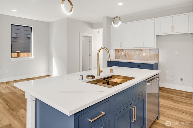 kitchen featuring a sink, blue cabinets, baseboards, stainless steel dishwasher, and white cabinetry