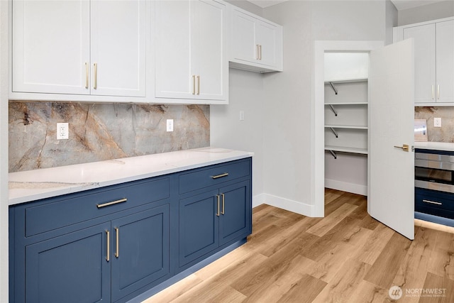 kitchen featuring blue cabinets, white cabinets, light wood-type flooring, baseboards, and decorative backsplash
