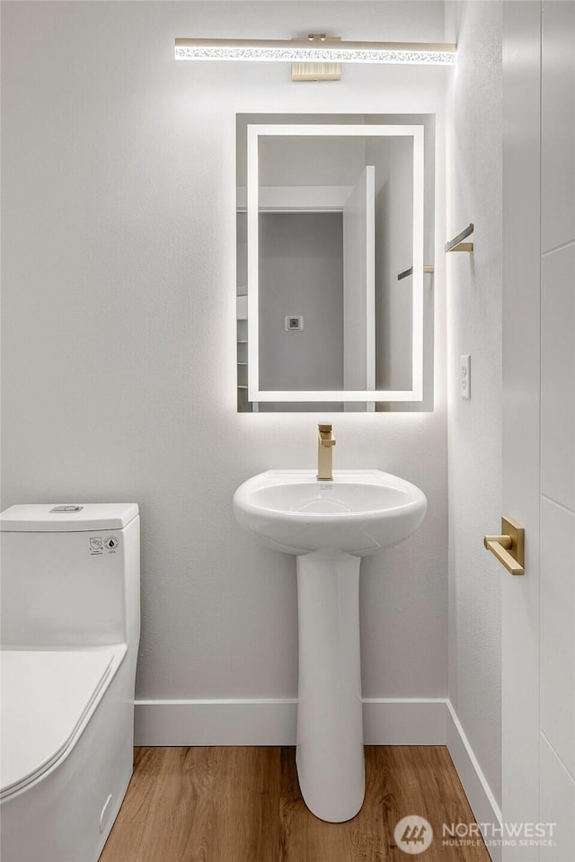 half bathroom featuring baseboards, wood finished floors, and toilet