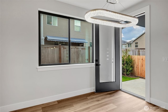 doorway to outside featuring a chandelier, baseboards, and wood finished floors