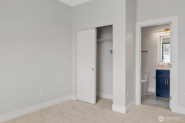unfurnished bedroom with a closet, baseboards, a sink, carpet floors, and ensuite bathroom