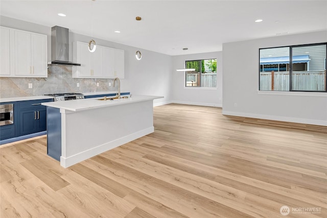 kitchen with a sink, wall chimney exhaust hood, open floor plan, blue cabinetry, and light countertops