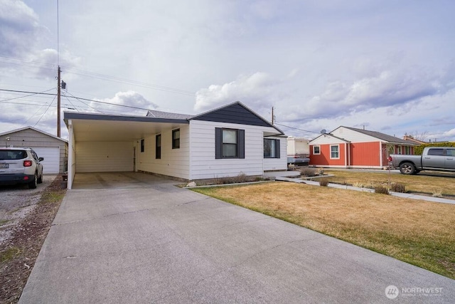 view of front of home featuring an attached carport, concrete driveway, an outbuilding, and a front yard