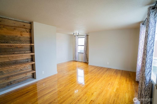 spare room with light wood-type flooring, baseboards, and a textured ceiling