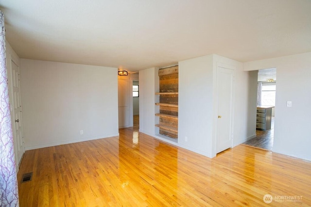 empty room with visible vents, built in shelves, baseboards, and light wood-style floors