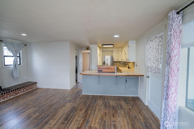 kitchen with a peninsula, stainless steel fridge with ice dispenser, a sink, dark wood-type flooring, and tasteful backsplash