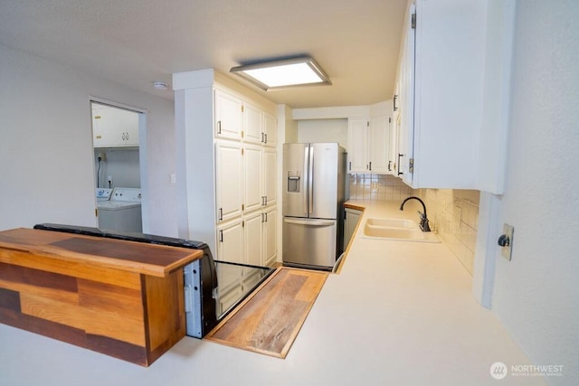 kitchen featuring backsplash, washer and dryer, stainless steel fridge, white cabinetry, and a sink