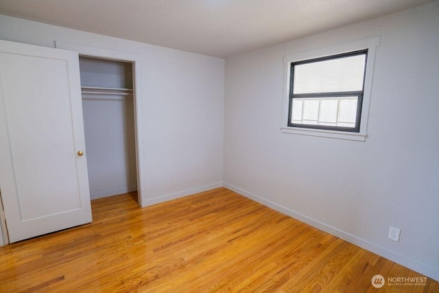 unfurnished bedroom featuring a textured ceiling, light wood-style floors, a closet, and baseboards