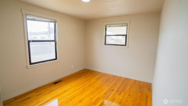 empty room with visible vents, light wood-type flooring, and baseboards